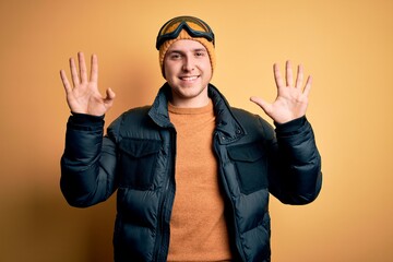 Young handsome caucasian man wearing hat, coat and ski glasses for winter and snow weather showing and pointing up with fingers number ten while smiling confident and happy.