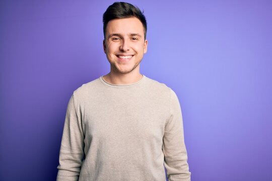 Young handsome caucasian man wearing casual sweater over purple isolated background with a happy and cool smile on face. Lucky person.
