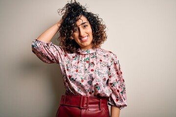 Young beautiful curly arab woman wearing floral t-shirt standing over isolated white background confuse and wonder about question. Uncertain with doubt, thinking with hand on head. Pensive concept.
