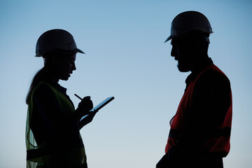 Silhouettes of an engineer with a tablet in his hands and a construction worker in a hard hat...