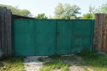Fototapeta premium old closed iron gate and part of a gray wooden fence on a rural street in green grass