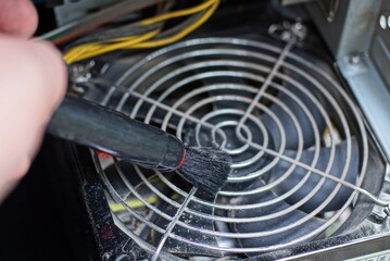 black brush in hand cleans dust on gray fan grill on computer