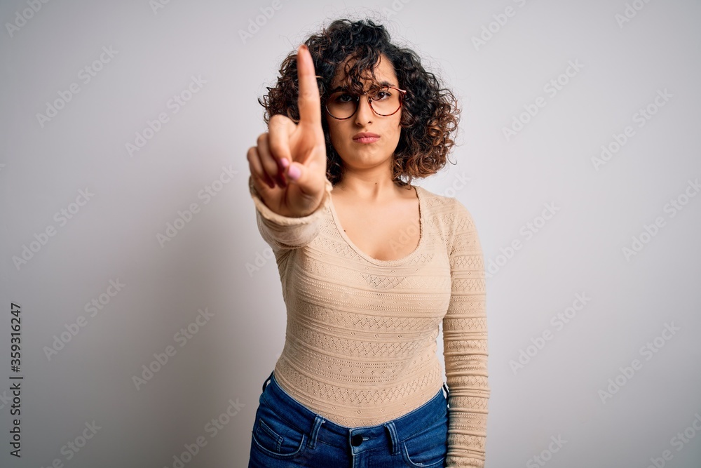 Sticker young beautiful curly arab woman wearing casual t-shirt and glasses over white background pointing w