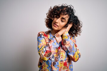 Young beautiful curly arab woman wearing floral colorful shirt standing over white background sleeping tired dreaming and posing with hands together while smiling with closed eyes.