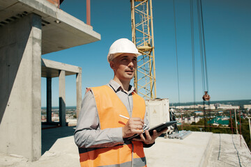 An engineer in an orange vest and a white construction control helmet conducts an inspection with a...