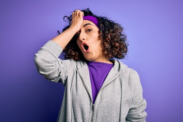 Beautiful curly arab sportswoman doing sport wearing sportswear over purple background surprised...