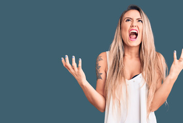 Young beautiful blonde woman wearing sleeveless t-shirt crazy and mad shouting and yelling with aggressive expression and arms raised. frustration concept.