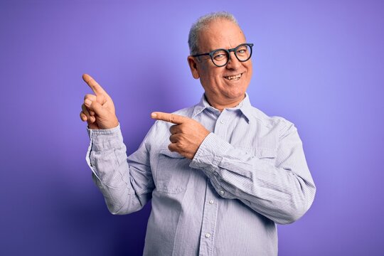 Middle age handsome hoary man wearing striped shirt and glasses over purple background smiling and looking at the camera pointing with two hands and fingers to the side.