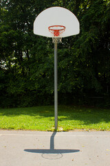 Picture of a basketball post with hoop, breakaway rim, backboard and net.  Image is taken in the concrete basketball field of an elementary school at midday.