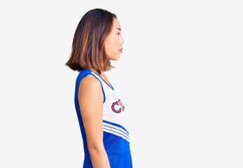 Young beautiful chinese girl wearing cheerleader uniform looking to side, relax profile pose with...