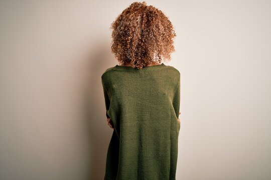 Beautiful african american woman with curly hair wearing casual sweater over white background standing backwards looking away with crossed arms