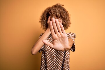 Young beautiful african american woman wearing casual shirt standing over yellow background...