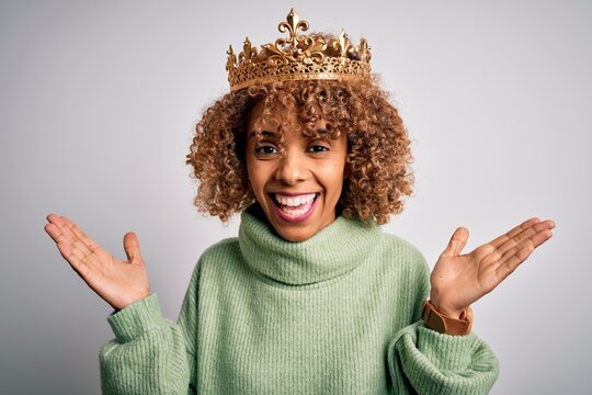 Young african american woman wearing golden crown of queen over isolated white background celebrating crazy and amazed for success with arms raised and open eyes screaming excited. Winner concept