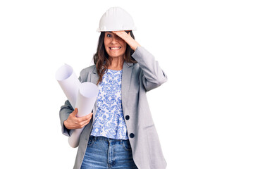 Young beautiful brunette woman wearing architect hardhat holding blueprint stressed and frustrated with hand on head, surprised and angry face