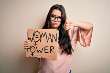 Young brunette woman holding women power protest banner over isolated background with angry face,...