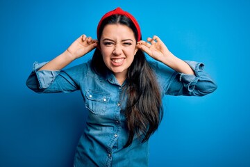 Young brunette woman wearing casual denim shirt over blue isolated background Smiling pulling ears with fingers, funny gesture. Audition problem