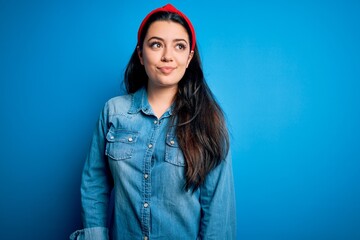 Young brunette woman wearing casual denim shirt over blue isolated background smiling looking to the side and staring away thinking.