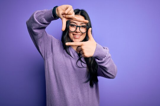 Young brunette woman wearing glasses over purple isolated background smiling making frame with hands and fingers with happy face. Creativity and photography concept.