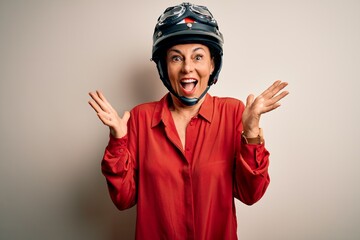Middle age motorcyclist woman wearing motorcycle helmet over isolated white background celebrating crazy and amazed for success with arms raised and open eyes screaming excited. Winner concept