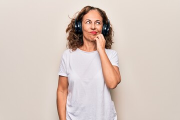 Middle age beautiful woman listening to music using headphones over white background thinking...