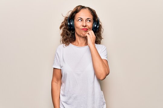 Middle age beautiful woman listening to music using headphones over white background thinking concentrated about doubt with finger on chin and looking up wondering