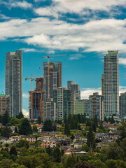 Fototapeta na wymiar Construction of New Residential District in the city of Burnaby, high-rise buildings under construction and construction cranes against the backdrop of blue cloudy sky and village in the foreground