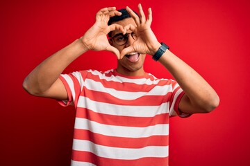 Young handsome african american man wearing casual striped t-shirt and glasses Doing heart shape with hand and fingers smiling looking through sign