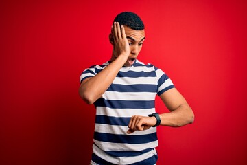 Handsome african american man wearing casual striped t-shirt standing over red background Looking...