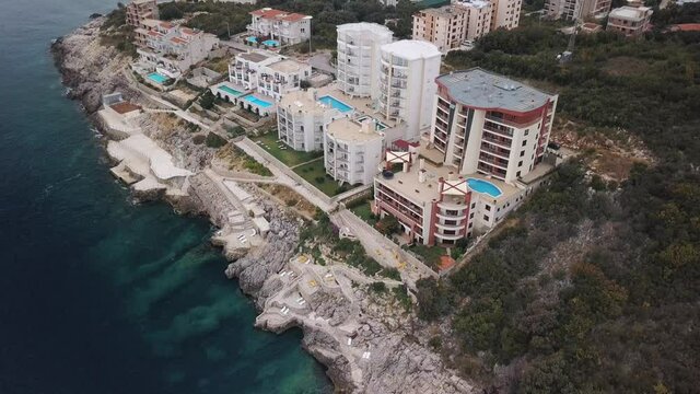 Aerial view of luxury hotels by the sea. Stock. Flying over the complex of hotels located on the stony sea shore on forested mountains background, concept of travelling and tourism.