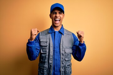 Young handsome african american handyman wearing worker uniform and cap celebrating surprised and amazed for success with arms raised and open eyes. Winner concept.