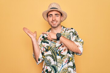 Young handsome man with blue eyes on vacation wearing summer florar shirt and hat amazed and smiling to the camera while presenting with hand and pointing with finger.