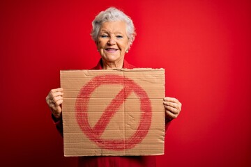 Senior beautiful grey-haired woman holding banner with prohibited signal over red background with a...