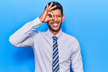 Young latin man wearing business clothes smiling happy doing ok sign with hand on eye looking through fingers