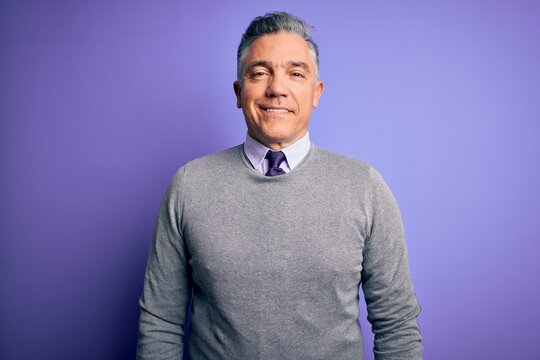 Middle age handsome grey-haired man wearing elegant sweater over purple background with a happy and cool smile on face. Lucky person.