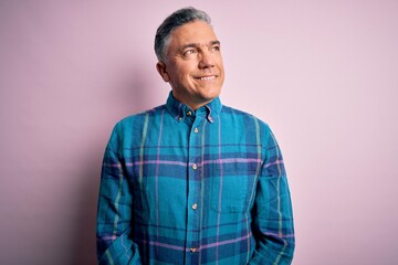 Middle age handsome grey-haired man wearing casual shirt over isolated pink background looking away to side with smile on face, natural expression. Laughing confident.