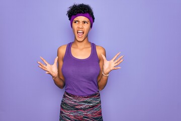 Beautiful african american afro woman wearing casual sportswear over purple background crazy and mad shouting and yelling with aggressive expression and arms raised. Frustration concept.