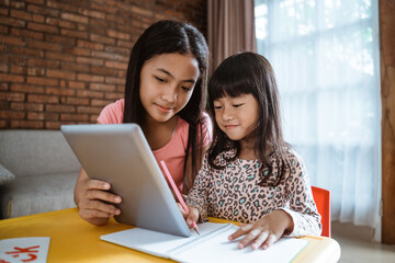 sister help making homework at home using tablet pc