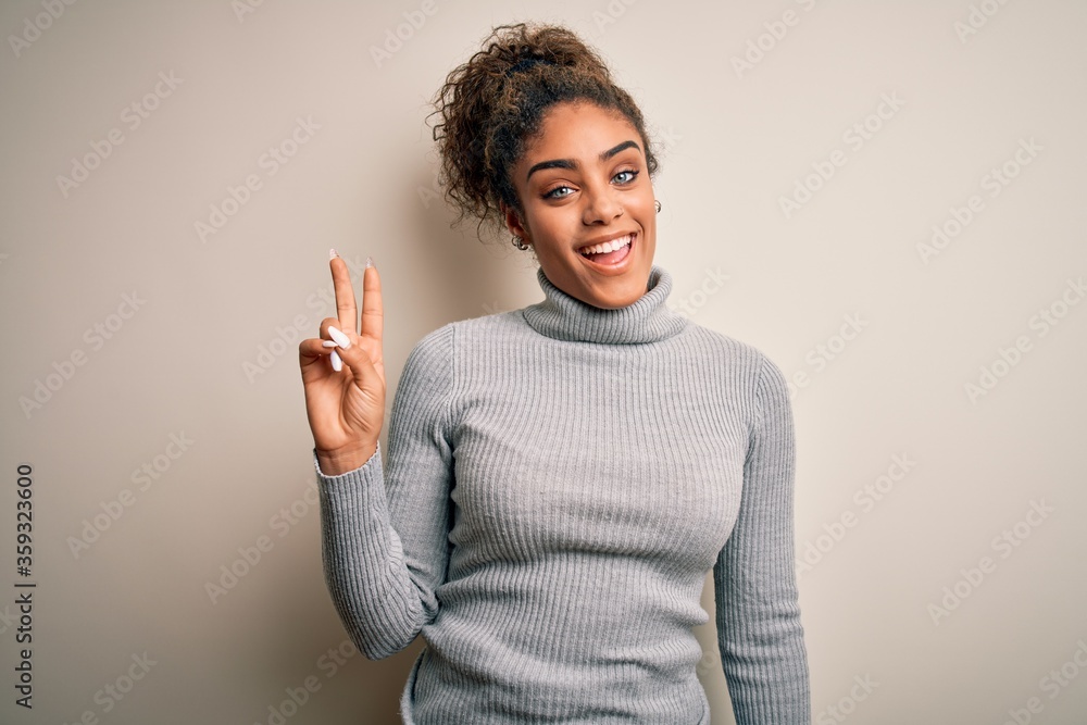 Sticker Beautiful african american girl wearing turtleneck sweater standing over white background showing and pointing up with fingers number two while smiling confident and happy.