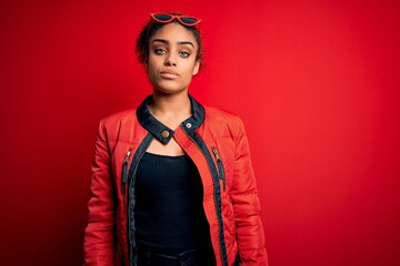 Beautiful african american girl wearing red jacket and sunglasses over isolated background Relaxed with serious expression on face. Simple and natural looking at the camera.