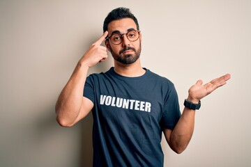 Handsome man with beard wearing t-shirt with volunteer message over white background confused and...