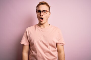 Young handsome redhead man wearing casual t-shirt standing over isolated pink background In shock...