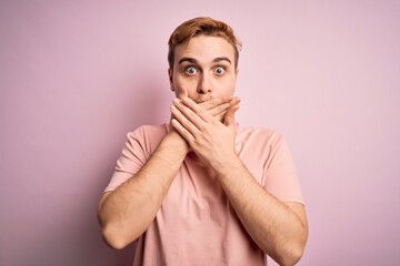 Young handsome redhead man listening to music using headphones over pink background shocked covering mouth with hands for mistake. Secret concept.