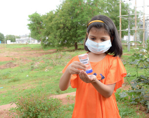 Little girl wearing medical protective mask during coronavirus and flu outbreak applies sanitizer for cleaning hands 