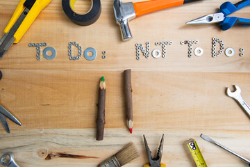 Top view of the phrases "to do" and "not to do" made of nuts and washers on a wooden surface for planning the work. Construction tools framing wooden background shot from above.