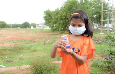 Little girl wearing medical protective mask during coronavirus and flu outbreak applies sanitizer for cleaning hands 