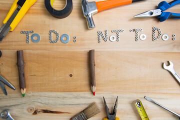 Top view of the phrases "to do" and "not to do" made of nuts and washers on a wooden surface for planning the work. Construction tools framing wooden background shot from above.