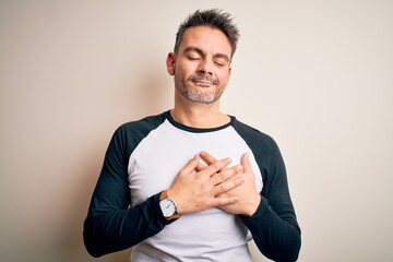 Young handsome man wearing casual t-shirt standing over isolated white background smiling with hands on chest with closed eyes and grateful gesture on face. Health concept.