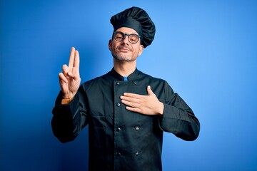 Young handsome chef man wearing cooker uniform and hat over isolated blue background smiling...