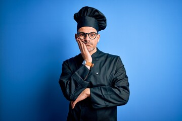 Young handsome chef man wearing cooker uniform and hat over isolated blue background thinking looking tired and bored with depression problems with crossed arms.