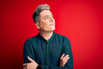 Obraz premium Young handsome modern man wearing elegant green shirt over red isolated background looking to the side with arms crossed convinced and confident